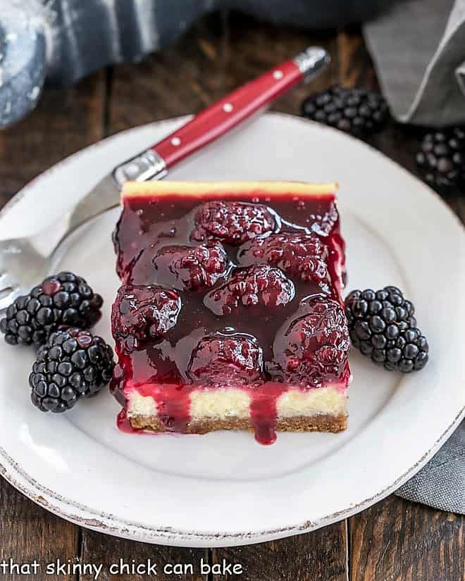 Blackberry Cheesecake Bars on a round white plate with fresh blackberries and a red handled fork.