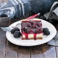 Black berry Topped cheesecake bar with fresh blackberries on a round white plate