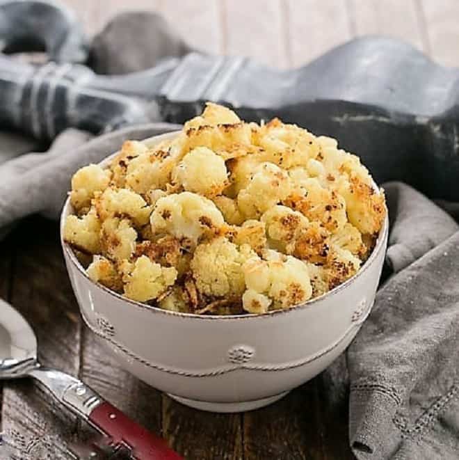Roasted cauliflower with Parmesan in a white ceramic bowl with a red handle serving spoon.
