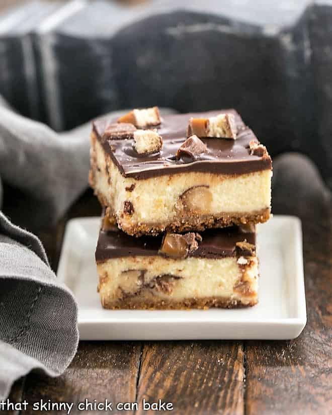 Two Twix Cheesecake Bars stacked on a square white plate