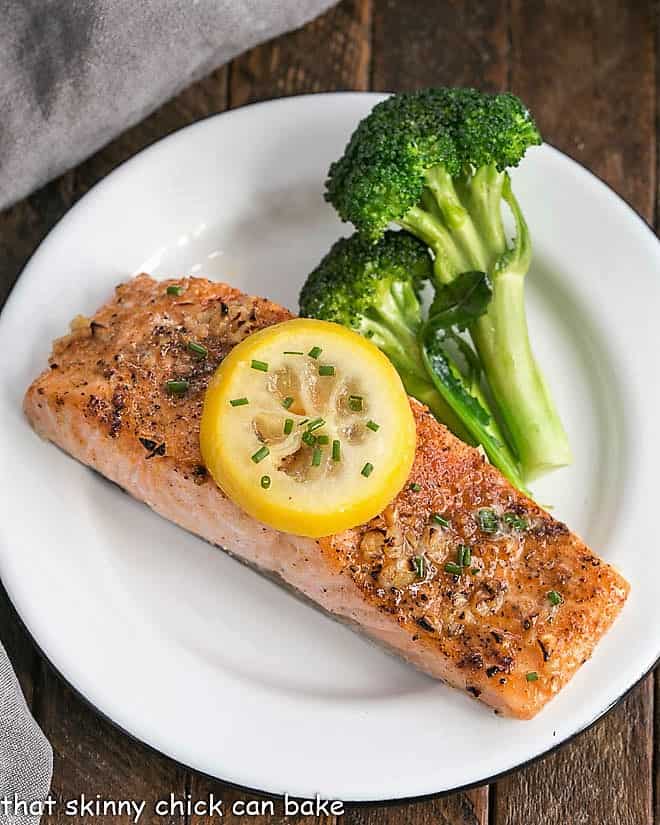 Overhead view of Salmon fillet topped with a lemon slice on a white plate with broccoli