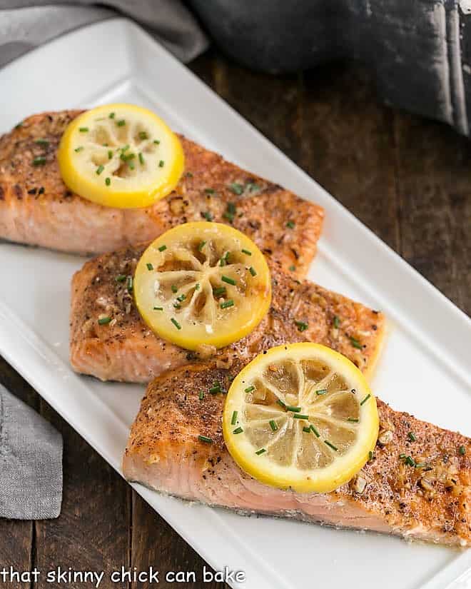 3 roasted salmon fillets topped with lemon slices on a white serving tray.