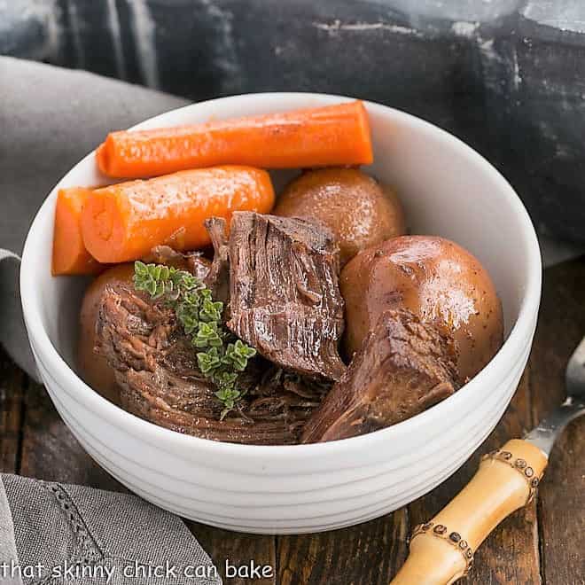 Instant Pot Beef Stew in a round white bowl with carrots and a sprig of thyme.