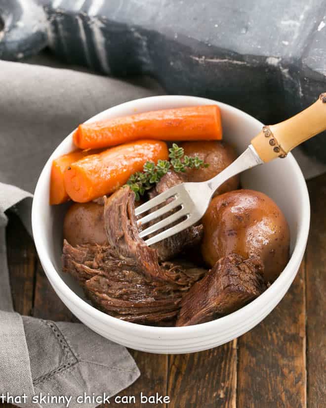 Pressure cooker beef stew in a white bowl with a fork piercing a piece of stew meat.