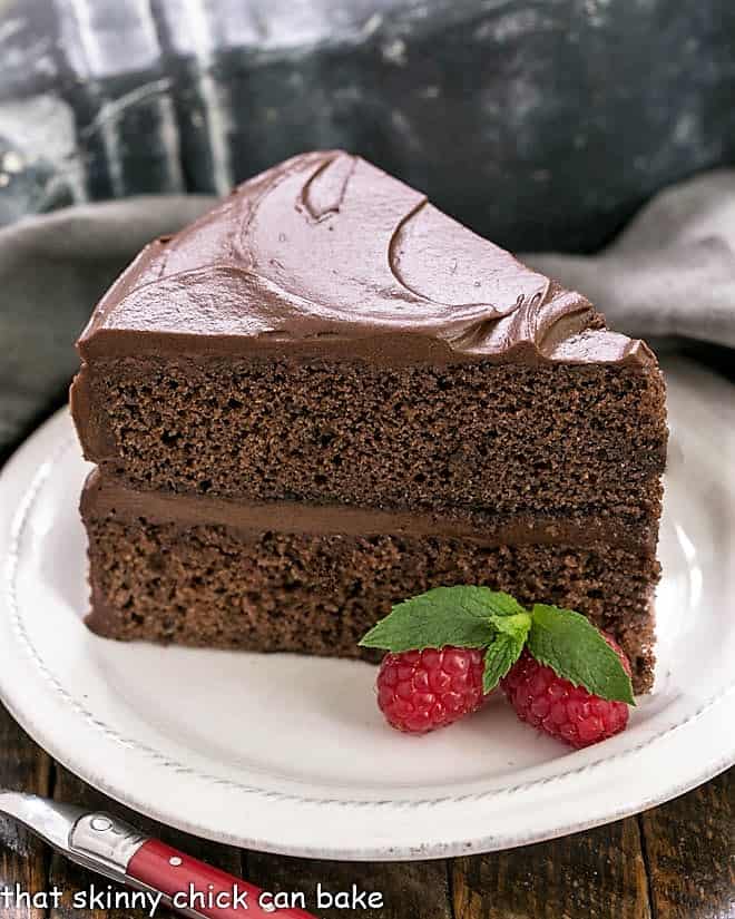 Slice of Devil's Food Cake on a white plate with berries and mint.