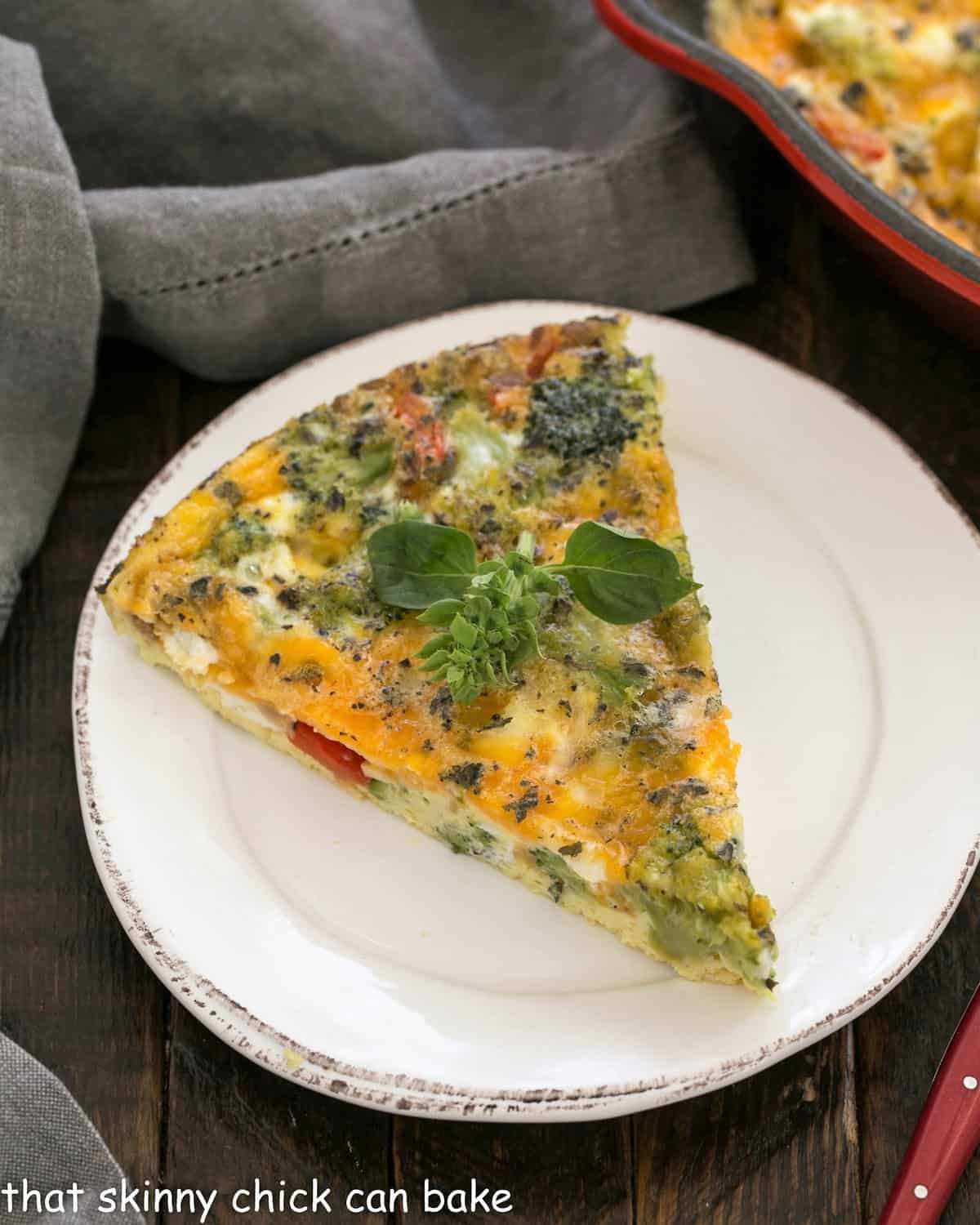 Overhead view of slice of broccoli frittata on a round white ceramic plate.