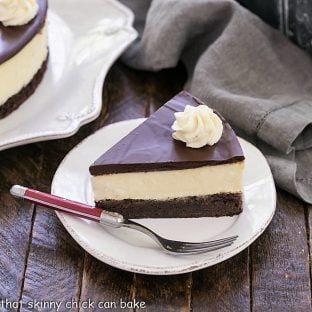 Slice of brownie cheesecake on a white dessert plate with a red handle fork