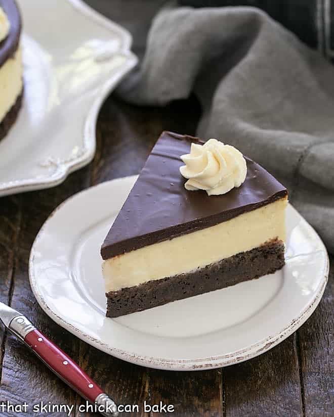 Slice of Baileys Brownie Cheesecake on a white dessert plate with a red handle fork.