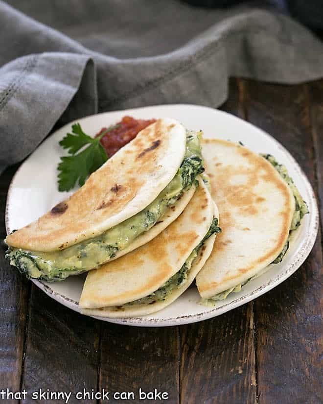 3 half quesadillas on a round white plate with a sprig of parsley and salsa.