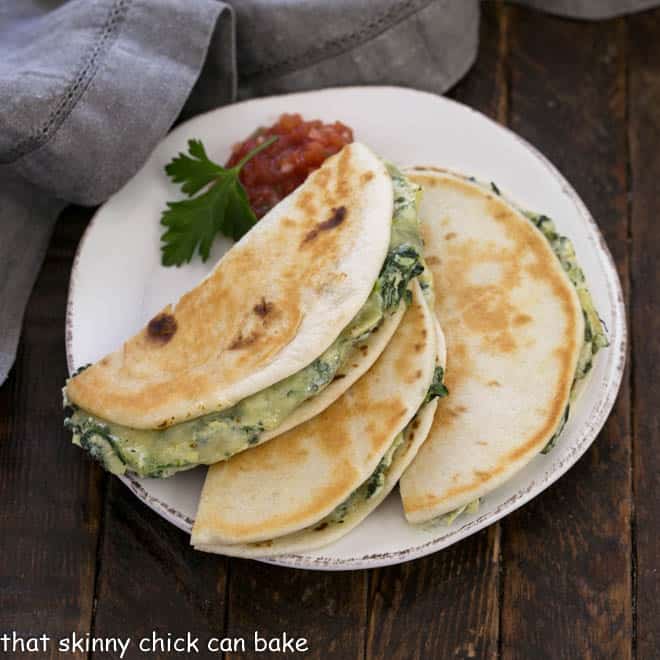 Overhead view of spinach dip quesadillas cut in half on a round white plate with salsa and a sprig of parsley