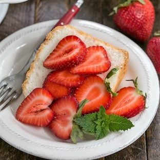 Slice of angel food cake on a white plate topped with berries