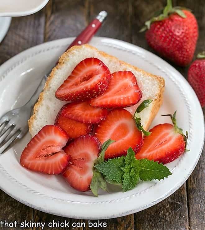 Slice of angel food cake on a white plate topped with berries