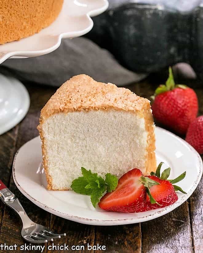 Slice of angel food cake on a white dessert plate with sliced strawberries and mink