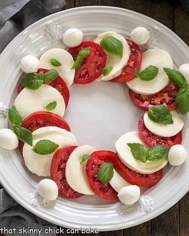 Slices of mozzarella and tomatoes on a platter with a few basil leaves