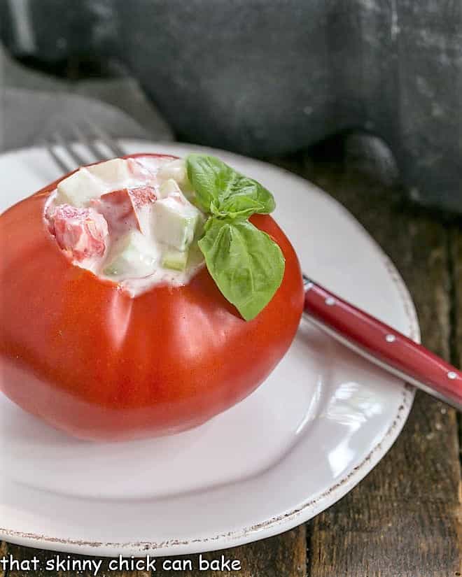 A salad stuffed tomato on a white plate with a red handled fork