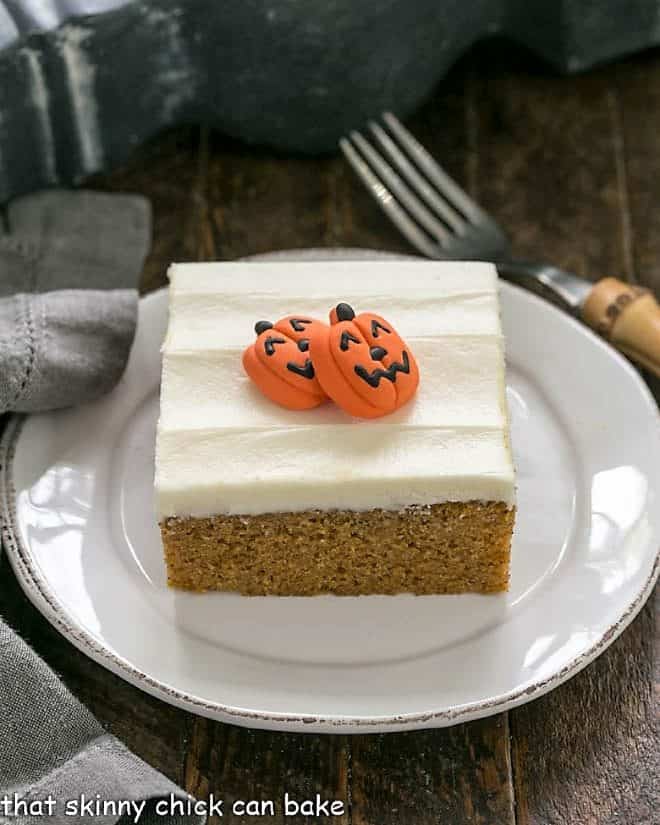 One pumpkin bar with cream cheese frosting and 2 sugar pumpkins to garnish on a round white dessert plate.