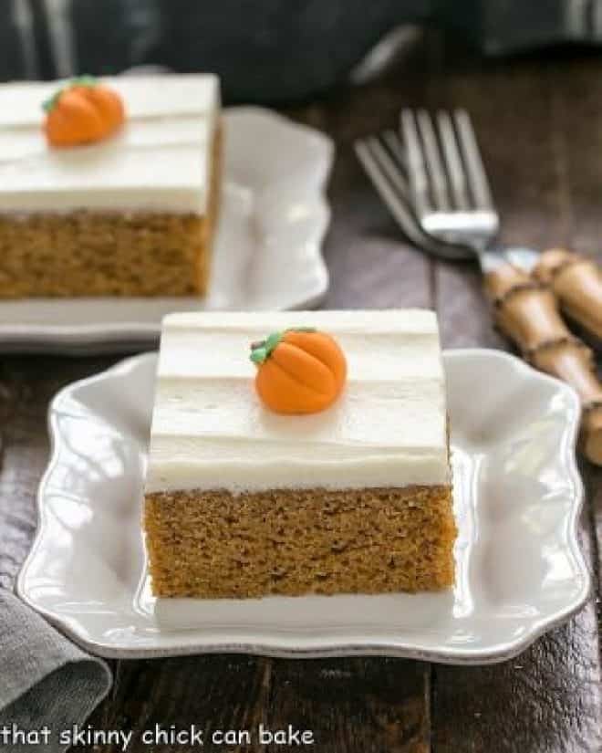 Two pumpkin bars with cream cheese frosting and candy pumpkins on white dessert plates.