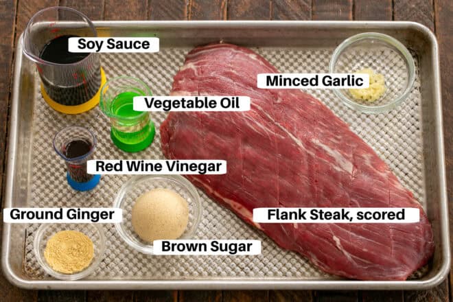 Ingrediennts for marinated grilled flank steak with labels on a sheetpan.