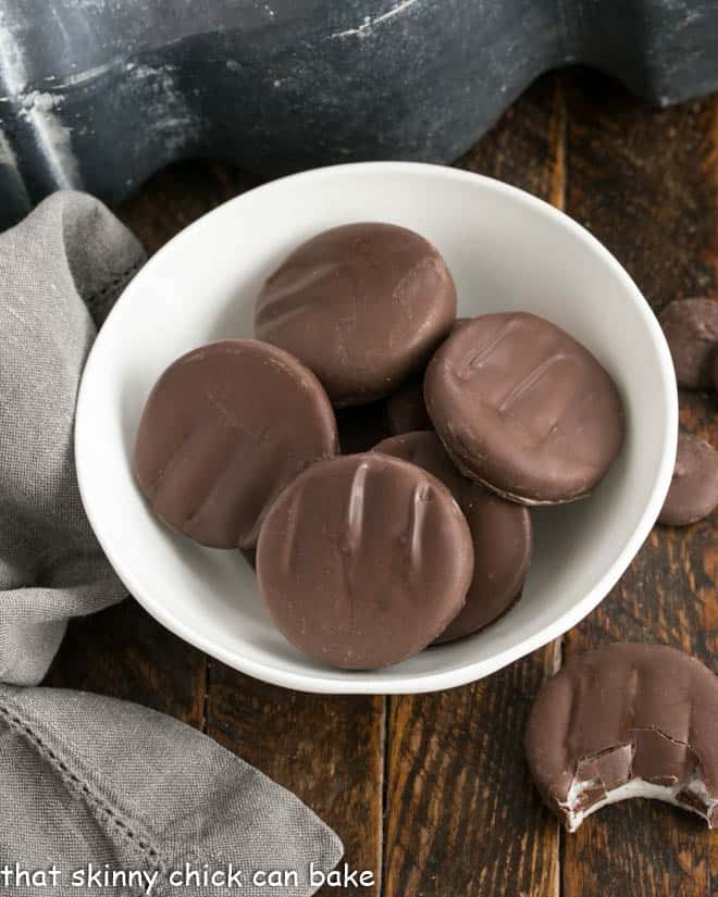 Overhead view of homemade Peppermint Patties in a white bowl with a bite removed from one on the counter