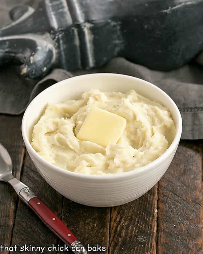 Homemade Mashed Potatoes with cream cheese are super creamy and perfect for a holiday dinner! Small bowl of homemade mashed potatoes in a white bowl with a red handled fork