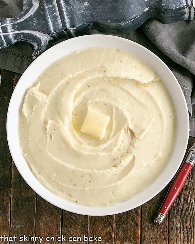 Homemdade Mashed Potatoes infused with butter, cream and cream cheese for a rich holiday or special occasion side dish! Overhead view of serving bowl of mashed potatoes with a pat of butter in the middle.