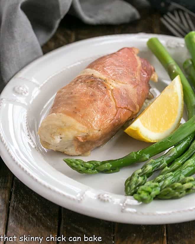 Boursin Chicken on a white plate with a lemon wedge and asparagus.