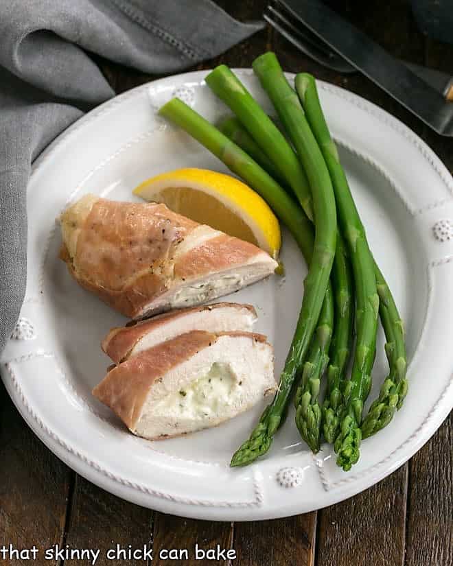 Overhead view of Boursin chicken slices a lemon and asparagus on a white dinner plate.