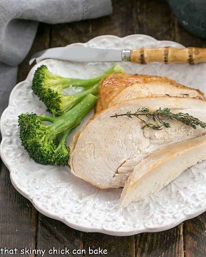 Rotisserie Style chicken slices on a white plate with a knife and broccoli spears.