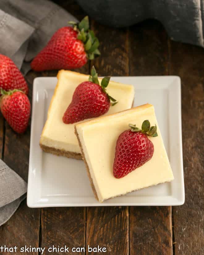 two cheesecake bars topped with strawberries on a square white plate