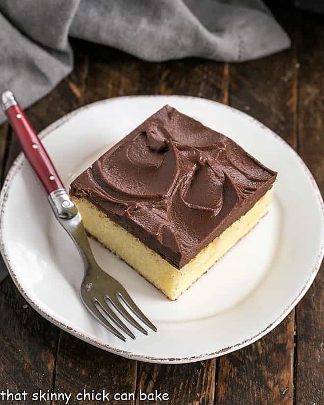 A square of one layer yellow cake on a round white dessert plate with a red handle fork