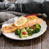 Oven roasted salmon topped with a lemon slice on a white plate with broccoli