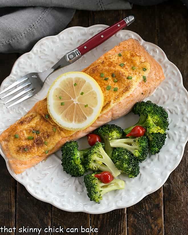 Overhead view of Roasted Salmon topped with a lemon slice on a white plate with broccoli