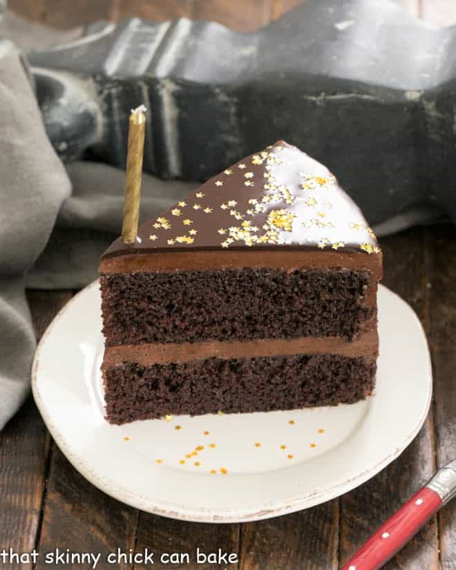 Glazed Chocolate Mirror cake slice with a candle on a dessert plate.