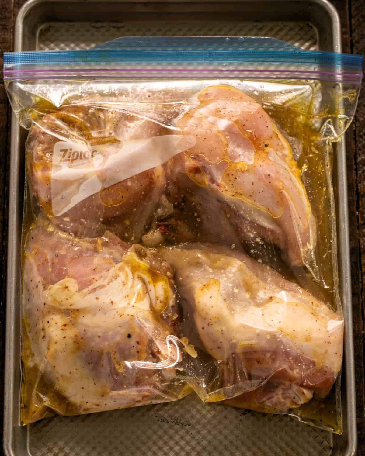 Chicken with marinade in a Ziploc bag on a sheetpan.