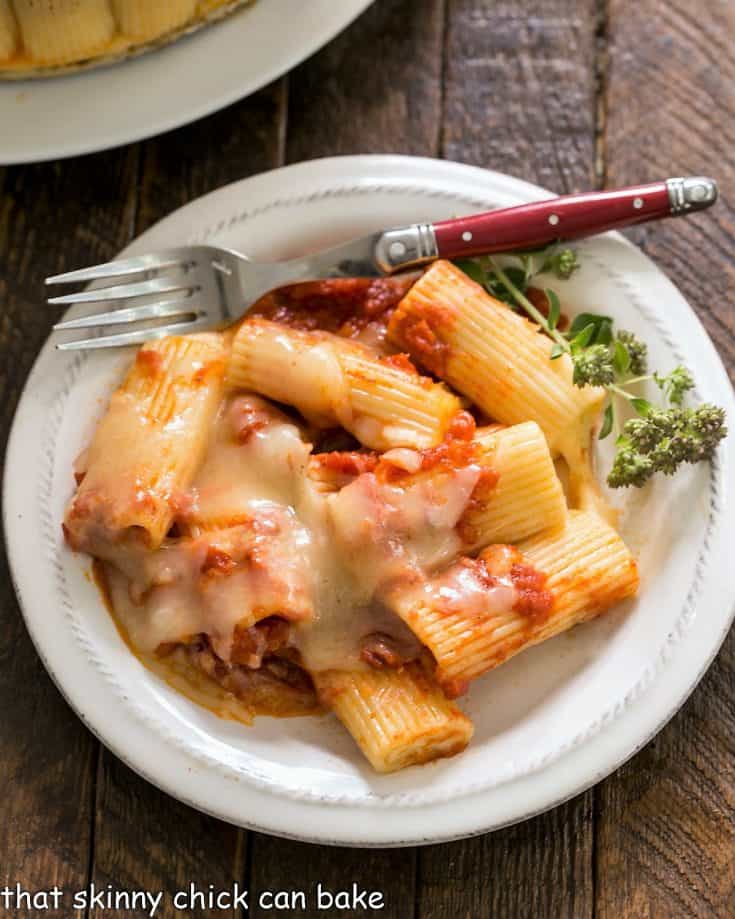 Overhead view of baked rigatoni on a small wite plate with a fork and herb garnish