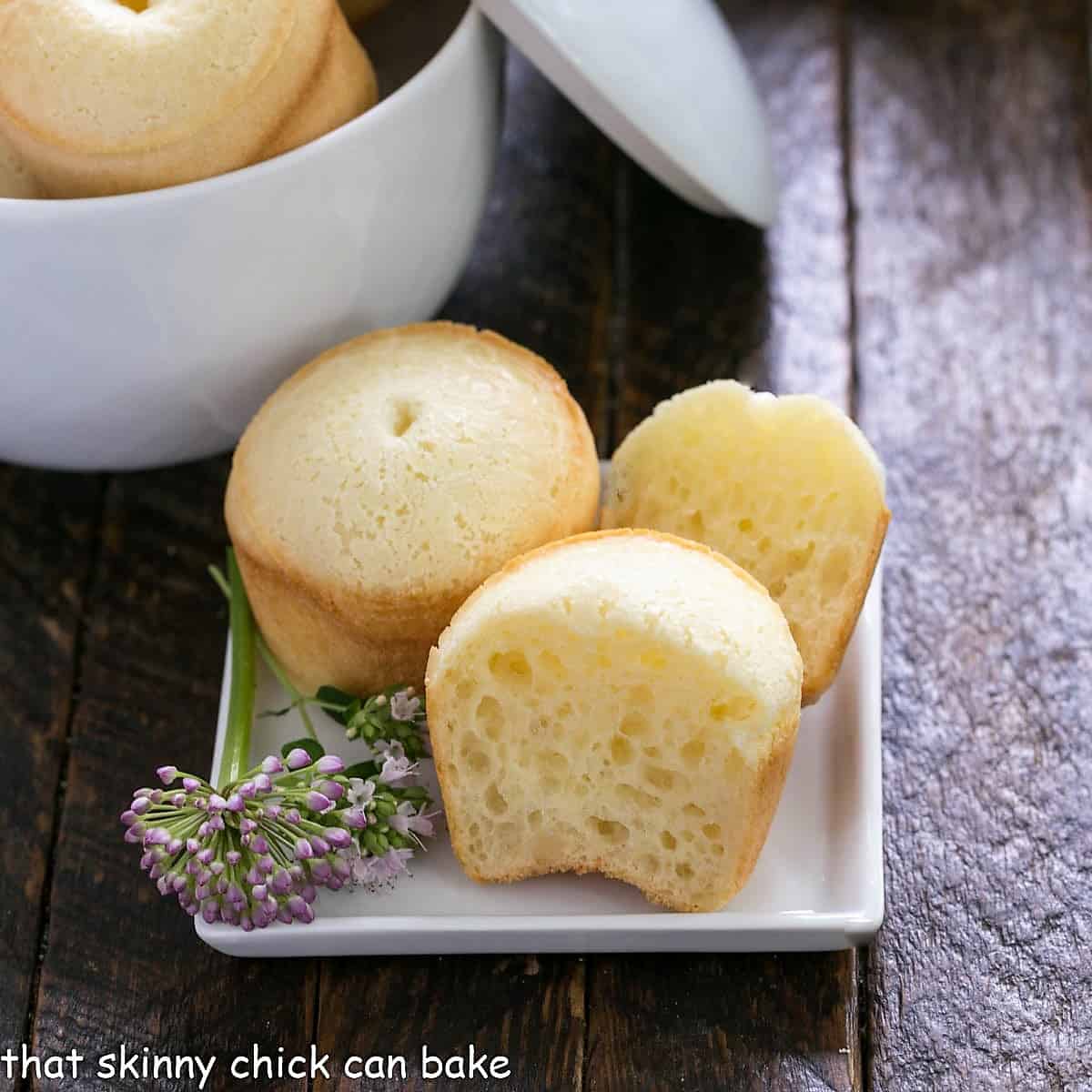 Sliced open Brazilian cheesebread on a white plate with a chive flower garnish.