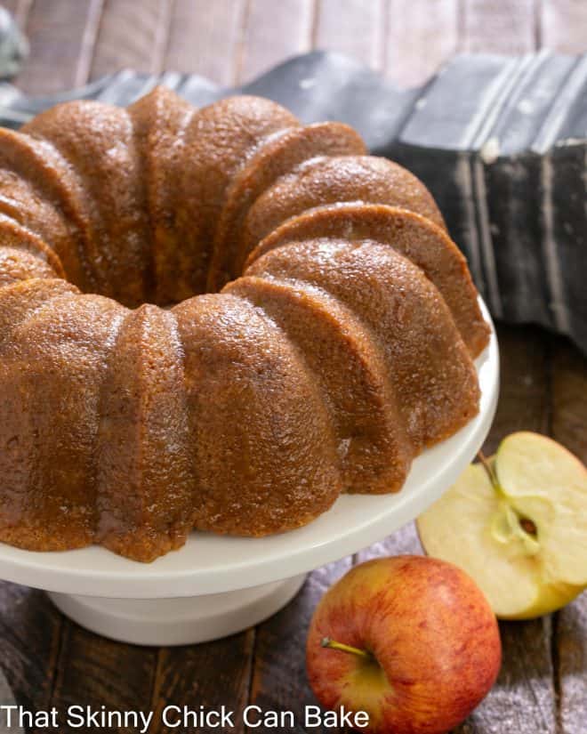 Apple Bundt Cake on a white cake stand next to 2 apples