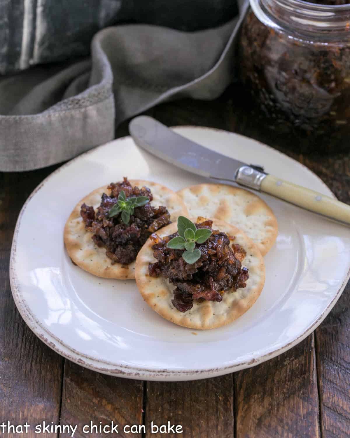 Bacon jam on crackers on a white appetizer plate.