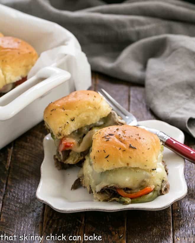 Two cheesesteak sliders on a white plate with a fork