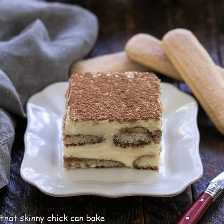 A slice of classic tiramisu on a square white plate with 2 ladyfingers