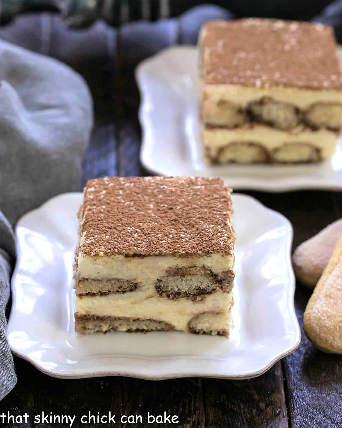 Two slices of tiramisu on square white plates with tips of 2 ladyfingers visible on the side.