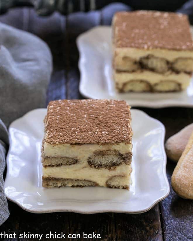 Two slices of tiramisu on square white plates with tips of 2 ladyfingers visible on the side
