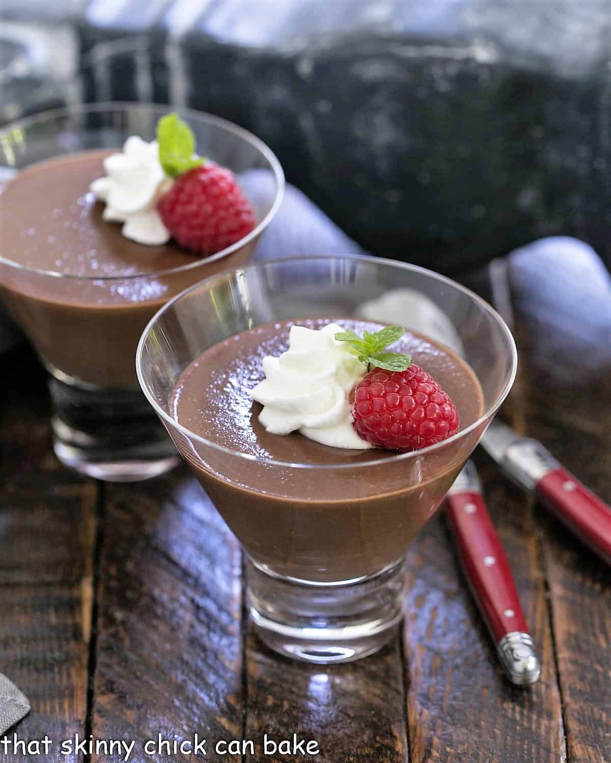 Italian chocolate pudding in 2 glass dishes topped with whipped cream, raspberries and mint