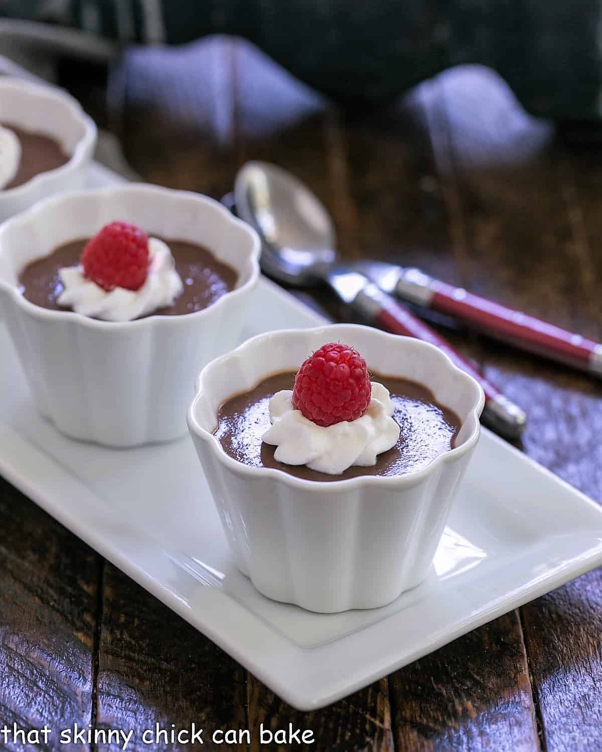 Budino in white ramekins topped with whipped cream and raspberries.