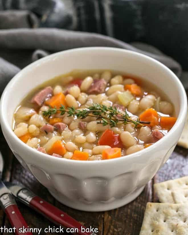 Navy bean soup in a white soup bowl with crackers and red handled spoons