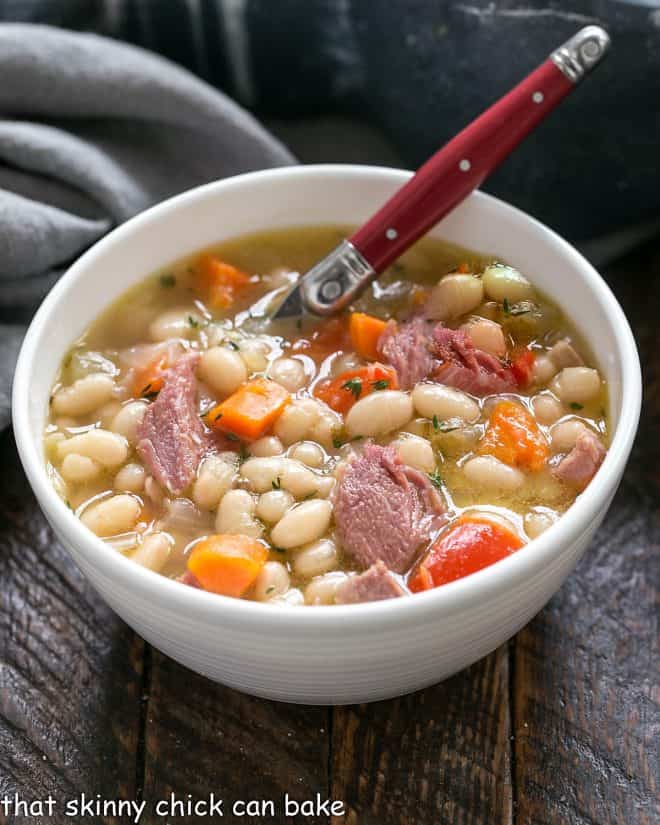 Old fashioned Navy Bean Soup in a white bowl with a red handled spoon