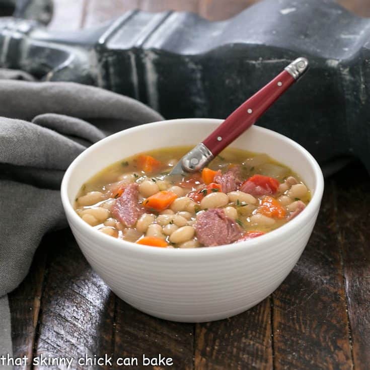 Bowl of bean soup in a white soup bowl with a red handled spoon