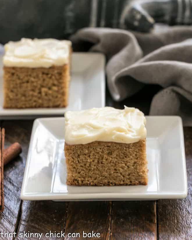 Two slices of frosted spice cake on square white plates.