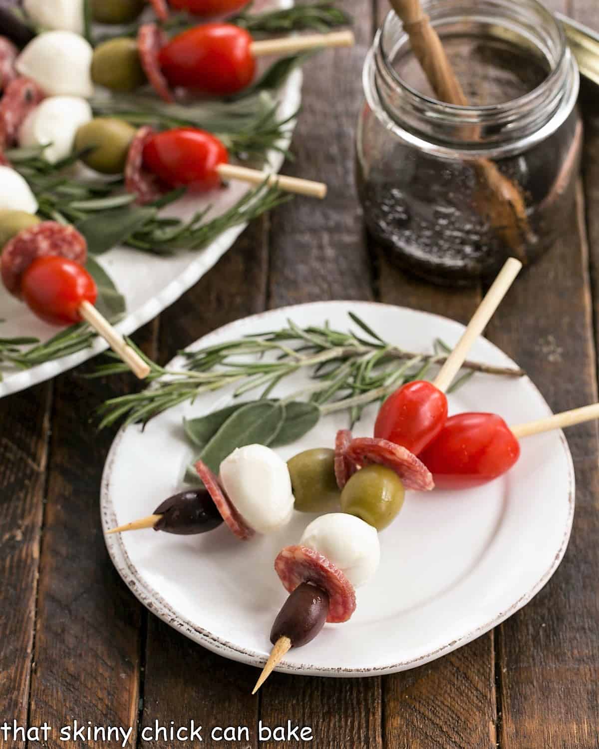 2 antipasto skewers on a white appetier plate with a garnish of rosemary.