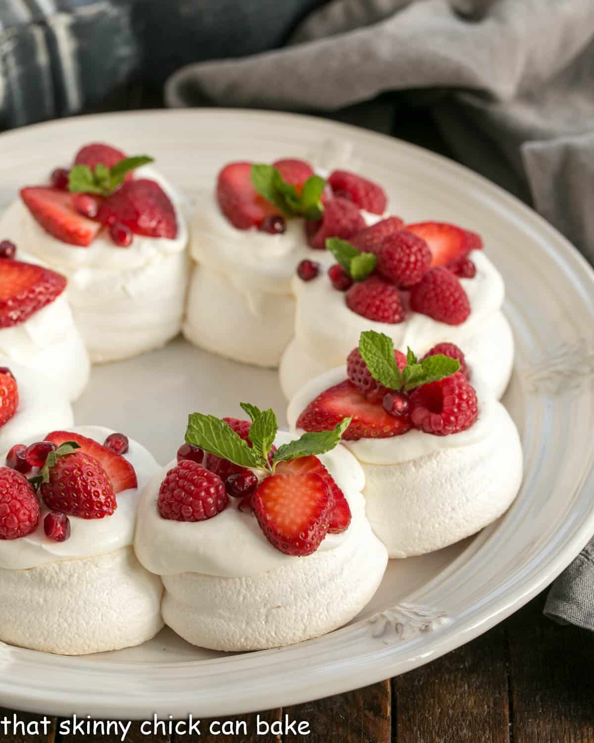 Pavlova Wreath topped with berries and cream on a white serving plate.